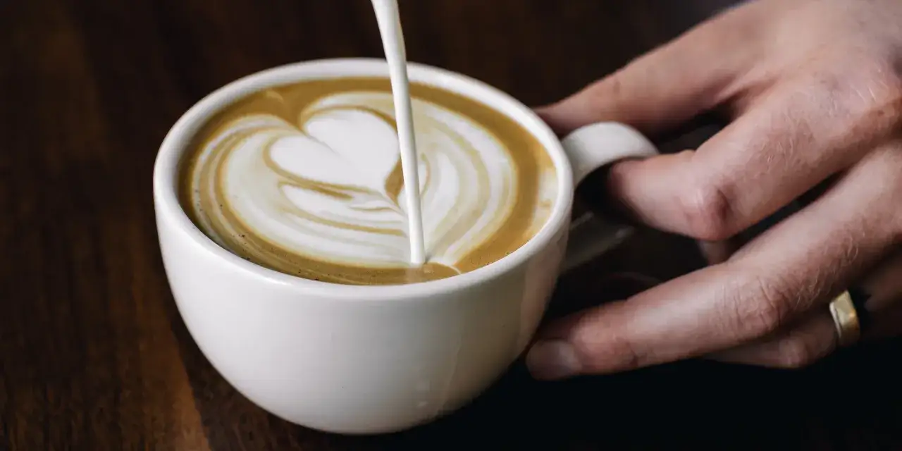 Un barista crea un cuore di latte art su un cappuccino, mostrando uno dei tanti tipi di cappuccino.