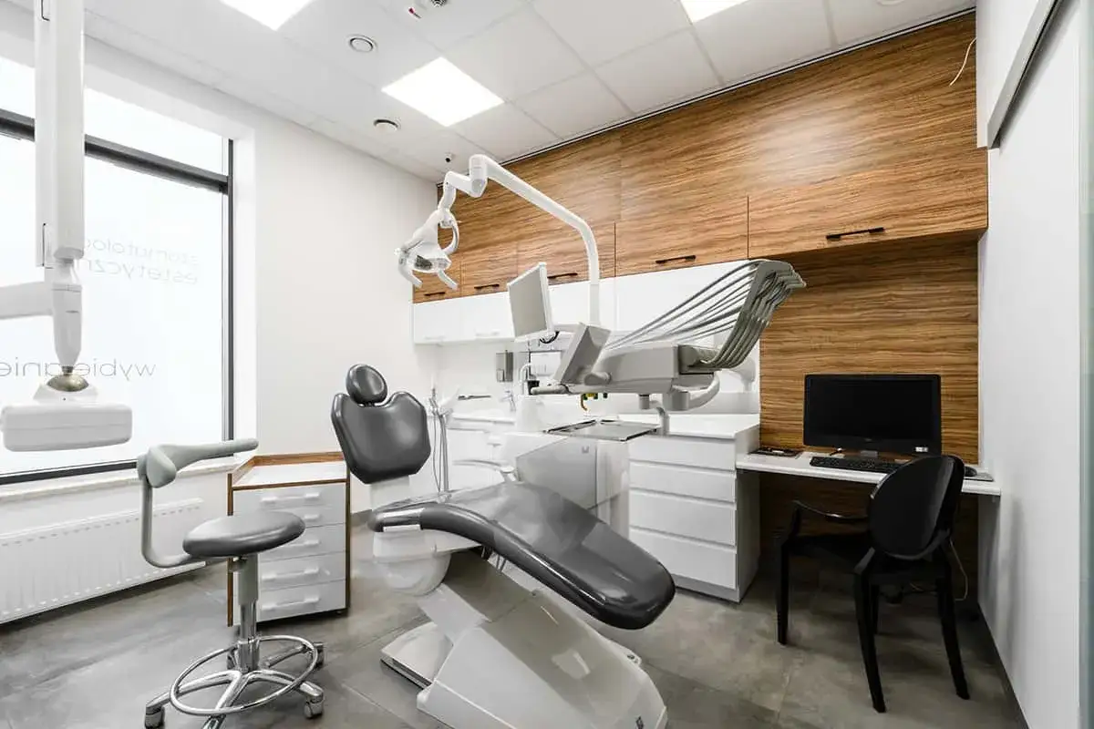 Nowoczesny gabinet stomatologiczny z fotelem dentystycznym, unitem i drewnianymi szafkami.