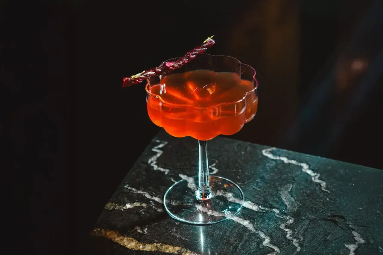 Elegancki drink z pomarańczowym płynem i ozdobnym patyczkiem. Czy to drink z dodatkiem bittersów?