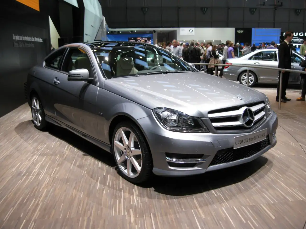 Silver Mercedes W204 coup&eacute; med soltak p&aring; en tr&auml;golvsm&auml;ssa.