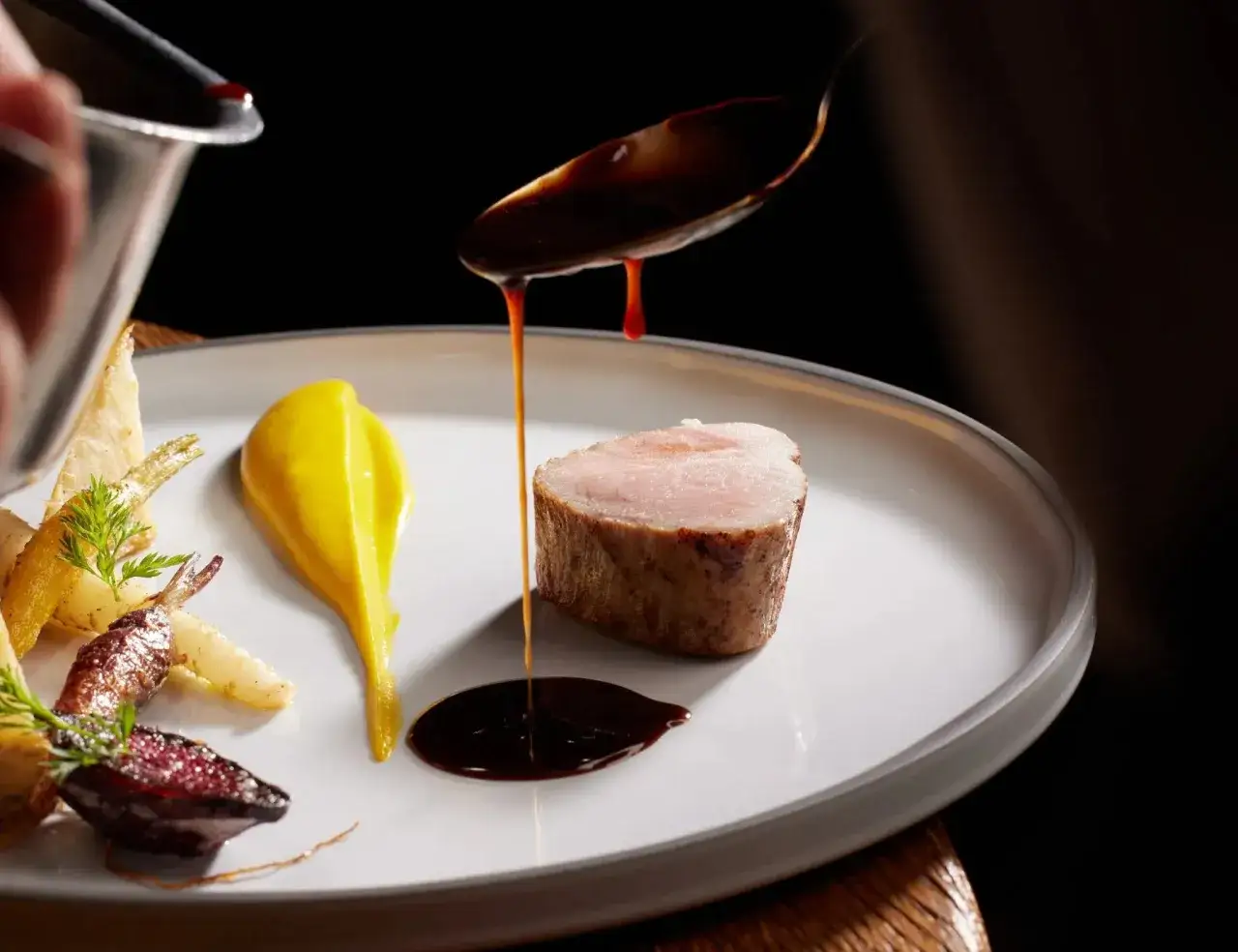 Une picanha de veau, sauce brune vers&eacute;e &agrave; la cuill&egrave;re, pur&eacute;e jaune et l&eacute;gumes racines sur une assiette blanche.
