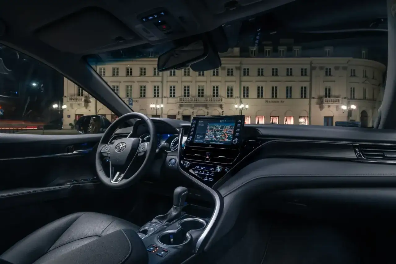 Wnętrze Toyoty Camry 2023 nocą, z widokiem na oświetloną kamienicę.
