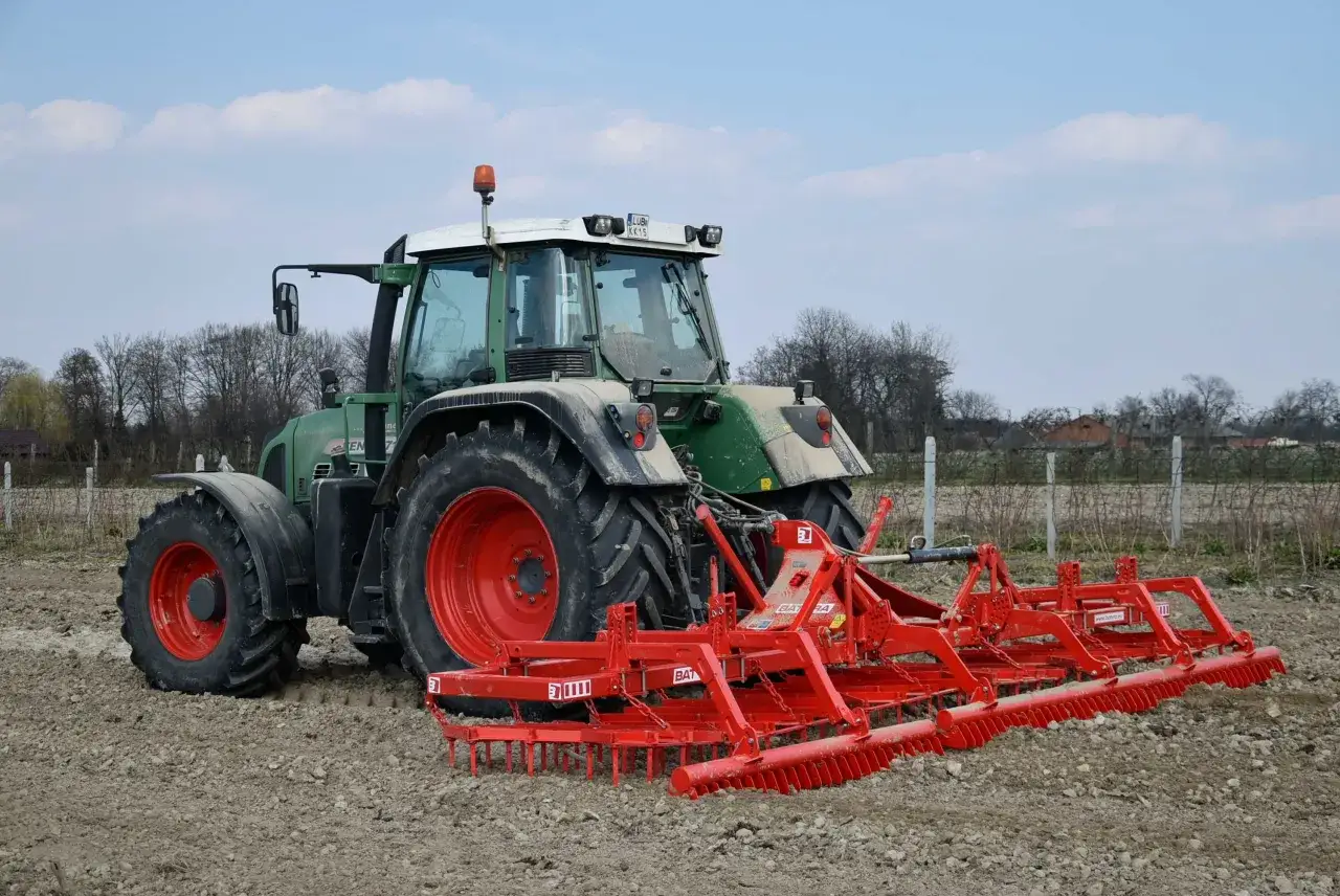 Zielony traktor z czerwoną broną gotową do pracy na polu.