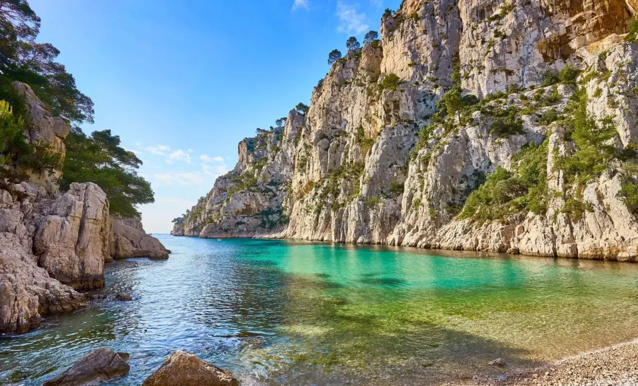 Turkusowa woda w zatoce otoczonej skalistymi klifami, porośniętymi zielenią. Widok na malownicze calanques w słoneczny dzień.