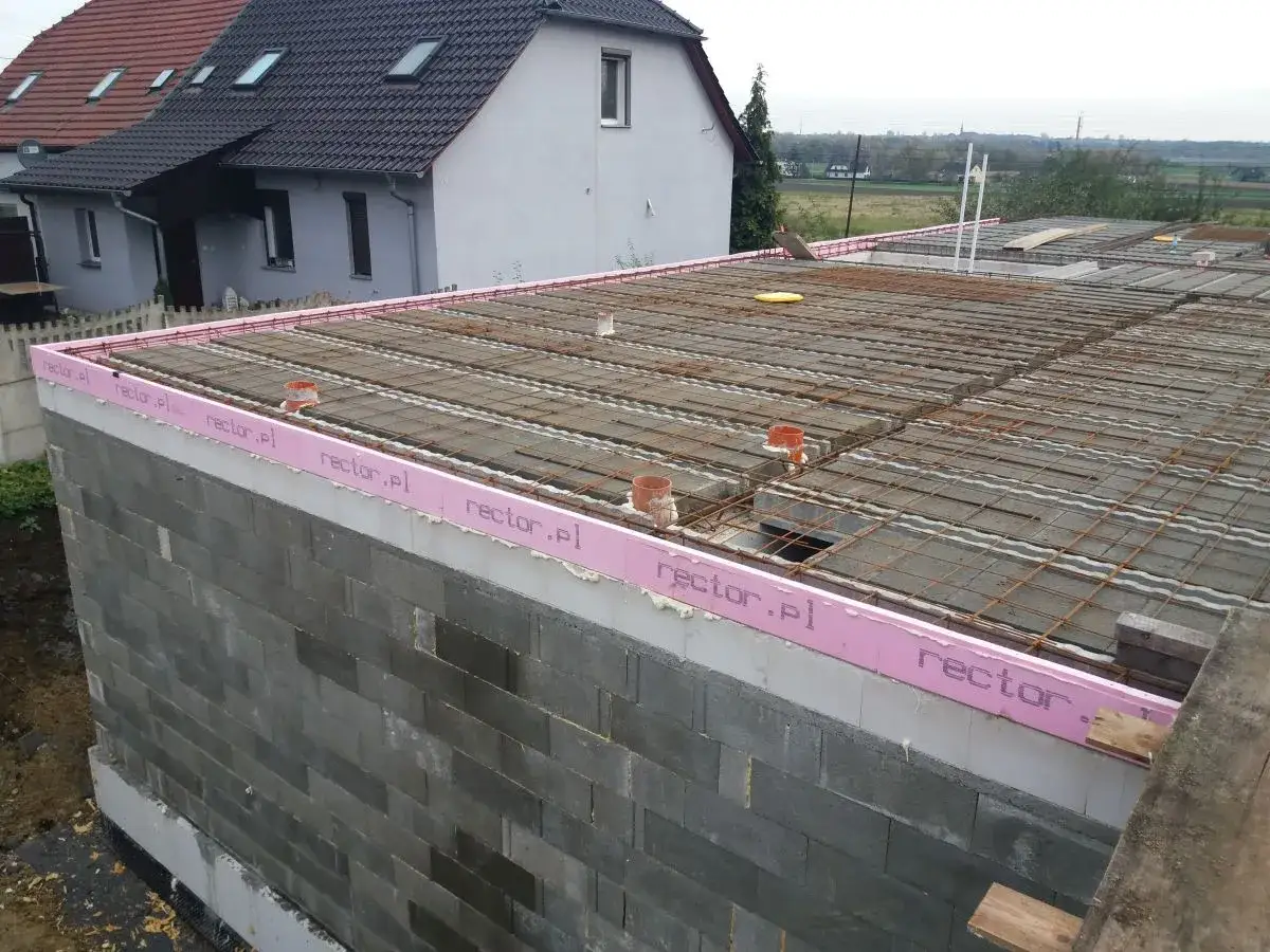 Budowa stropu zbrojonego, widoczne pustaki, styropian z napisem rector.pl i elementy instalacji.