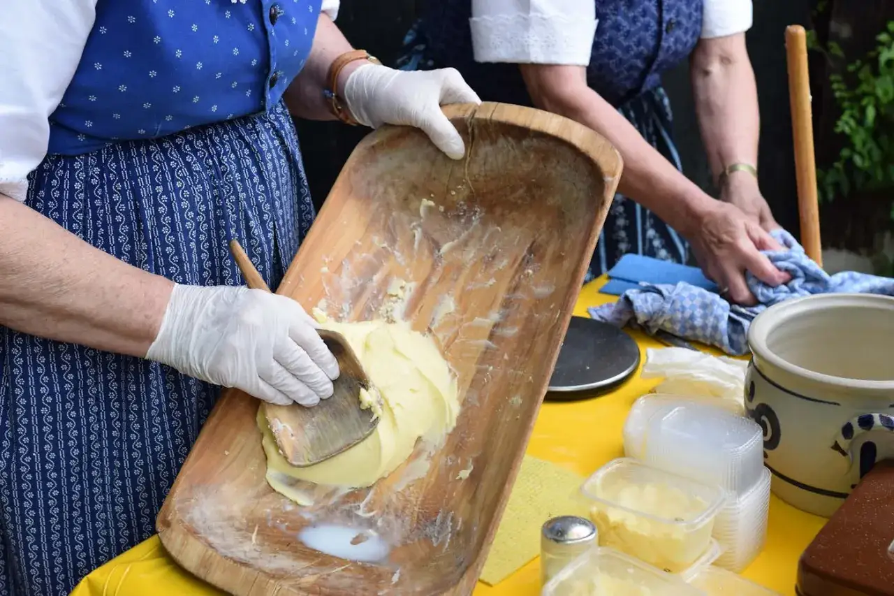 Hände mit Handschuhen verarbeiten Butter in einer Holzschale. Seit wann gibt es Butter? Wahrscheinlich seit der Jungsteinzeit, wie diese traditionelle Zubereitung zeigt.