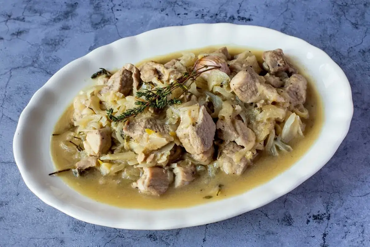 Deliciosa blanqueta de cerdo en salsa cremosa con cebolla y hierbas arom&aacute;ticas, servida en plato blanco.