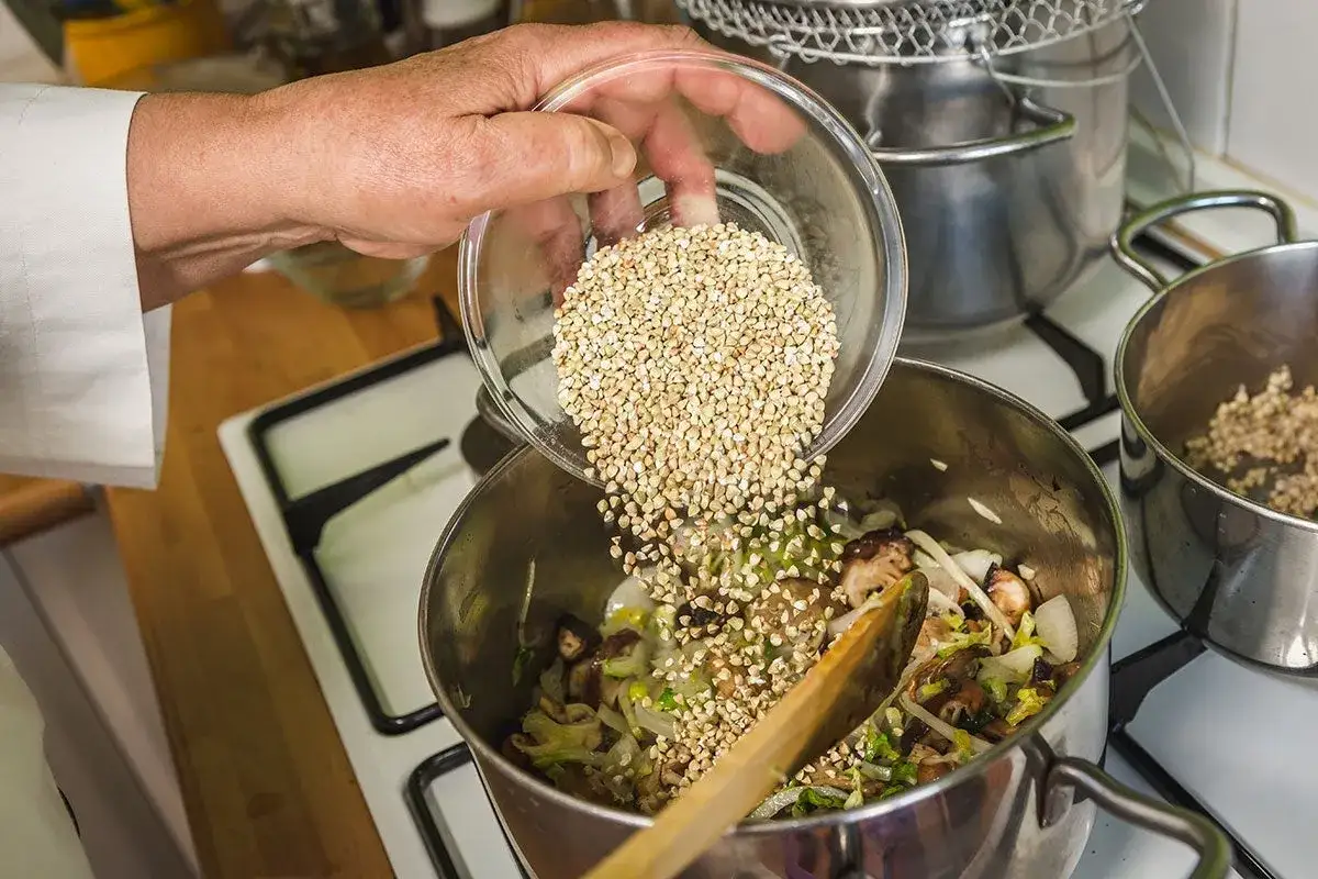 Mano añade trigo sarraceno a una olla con verduras.