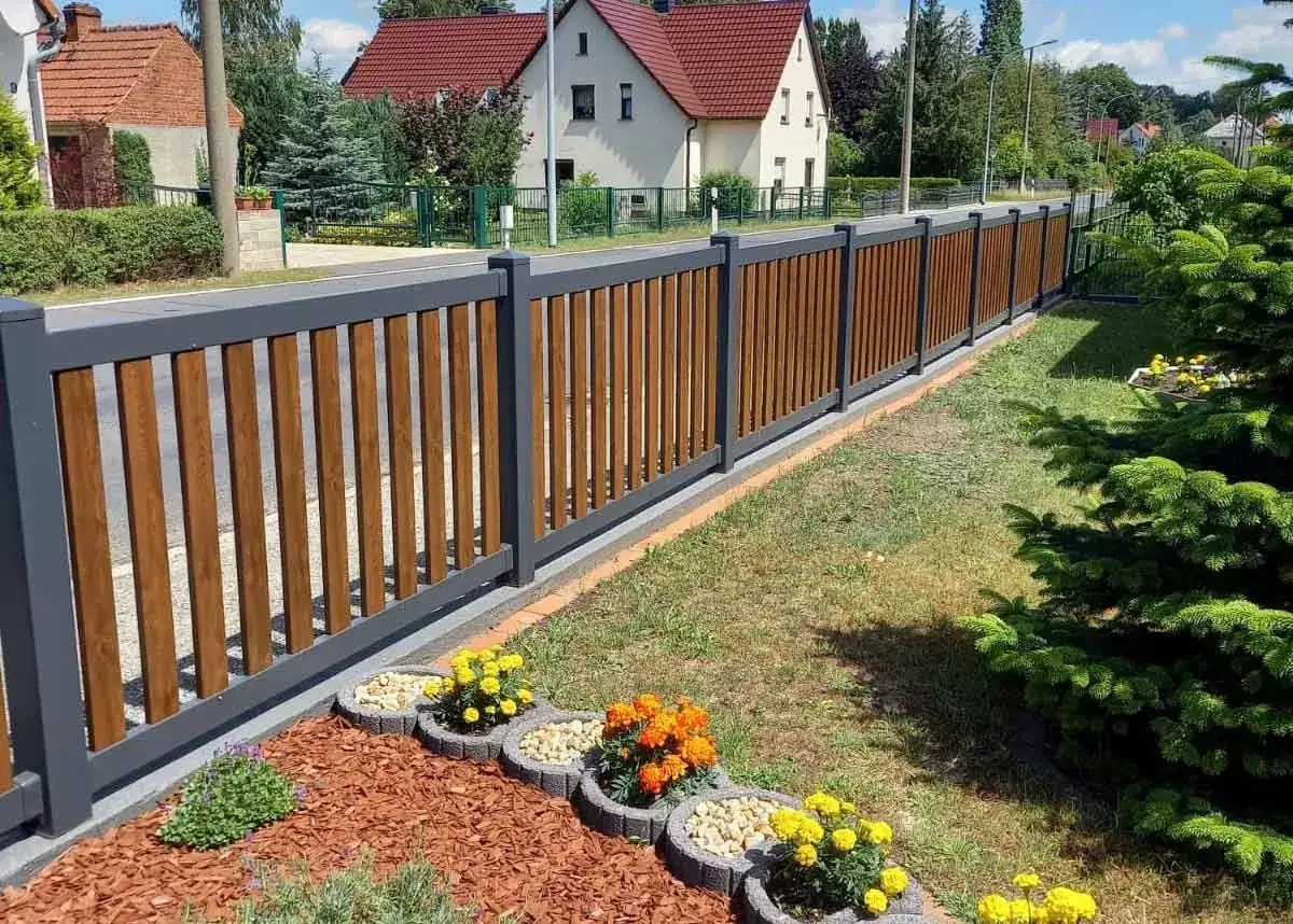 Moderne gartenzaun ideen bilder: ein dunkelgrauer Zaun mit Holzoptik-Paneelen, davor bunte Blumen und Rindenmulch.