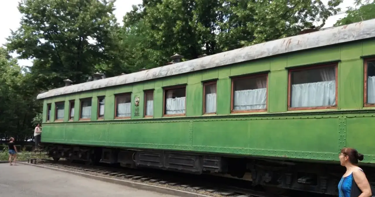 Zielony wagon kolejowy, część muzeum Stalina, z białymi zasłonami w oknach.