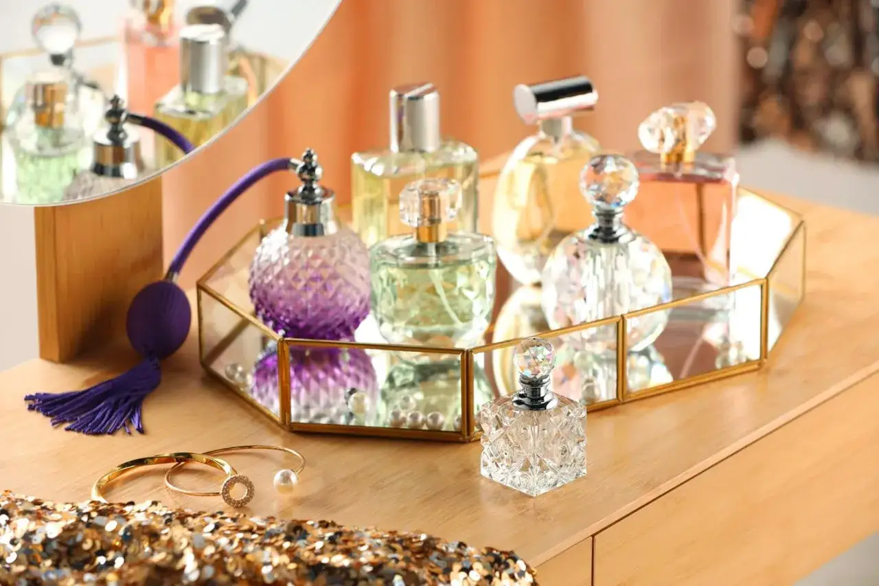 Eleganckie perfumy w ozdobnych flakonach, w tym fioletowy perfum z pompką, stoją na lustrzanej tacy.