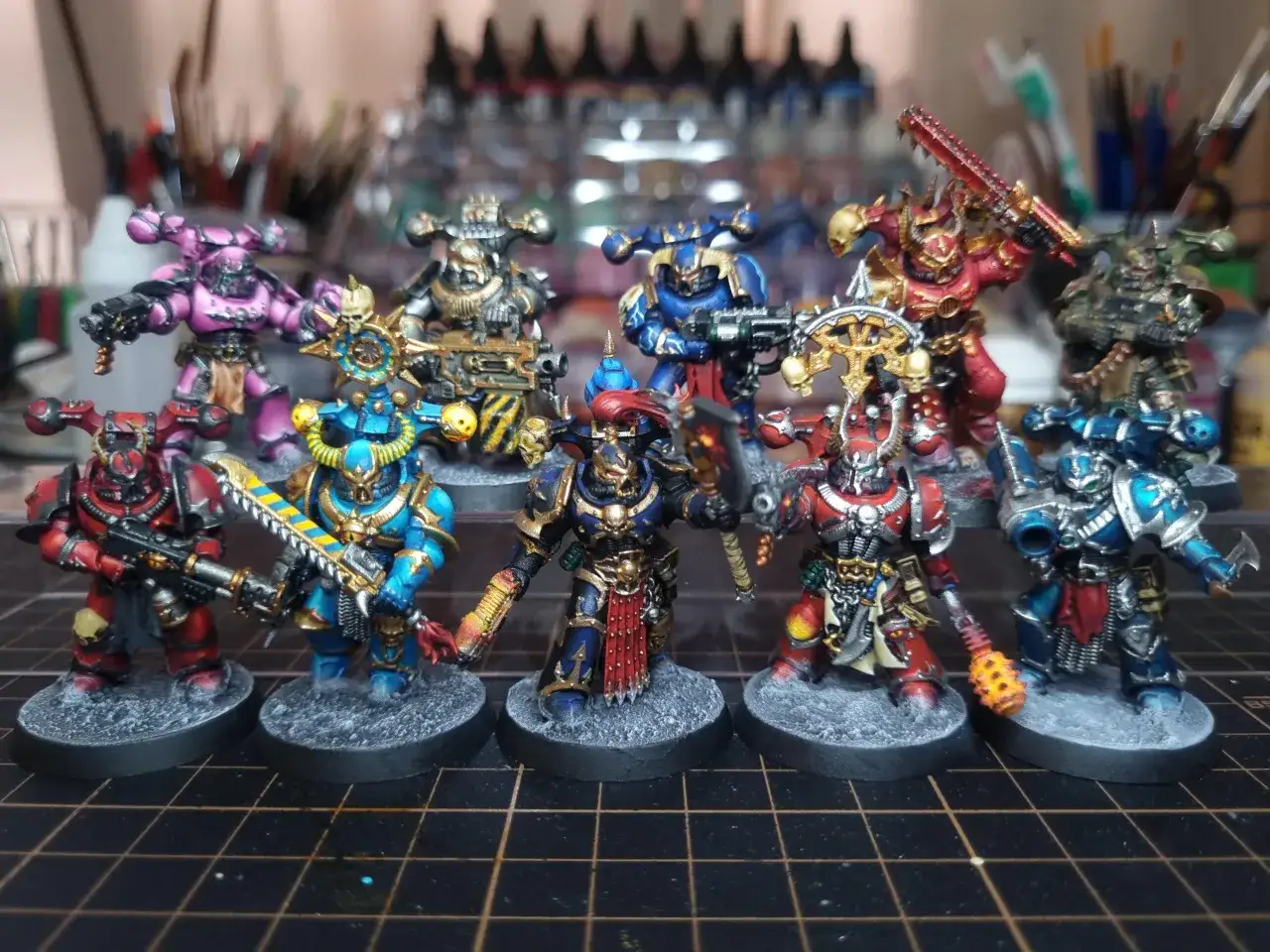 Dziesięciu pomalowanych wojowników Warhammer Chaos Legions w różnych kolorach, gotowych do bitwy.