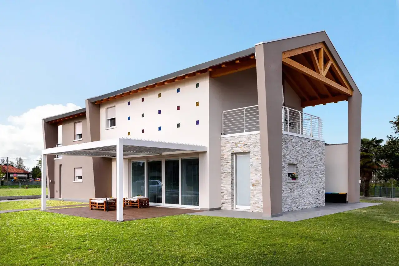 Casa moderna con tetto in legno a vista, facciata con inserti colorati e pietra.
