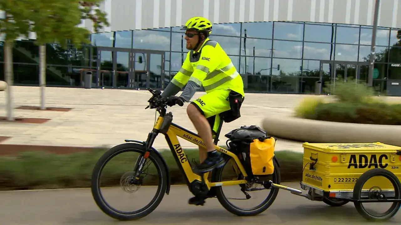 ADAC-Mitarbeiter auf gelbem Fahrrad mit Anhänger, bereit für eine Fahrradpanne.