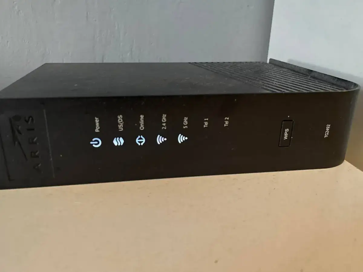 Czarny router Arris z widocznym przyciskiem WPS. Obok niego znajdują się wskaźniki Power, US/DS, Online, 2.4 GHz, 5 GHz, Tel 1 i Tel 2.