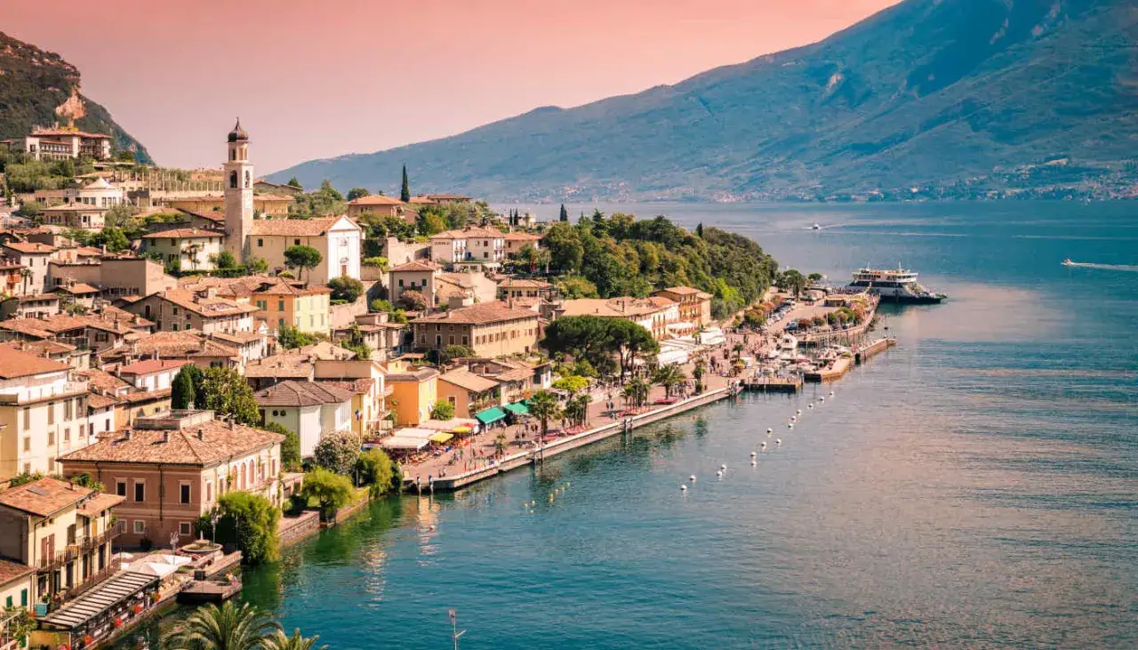 Vista panoramica di un pittoresco borgo sul Lago di Garda, con case colorate, un campanile e un lungolago animato. Perfetto per scoprire cosa vedere sul Lago di Garda.