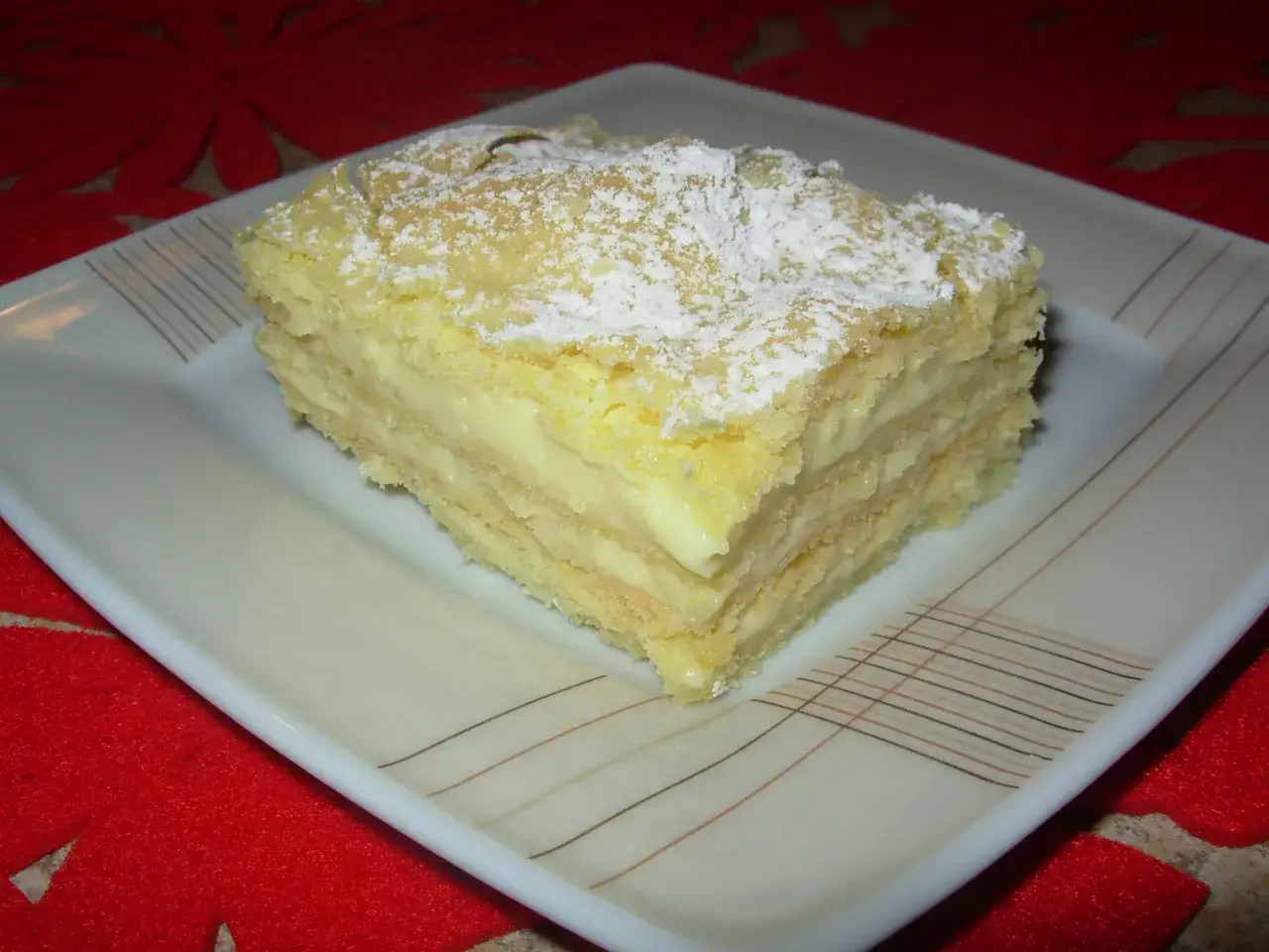 Pyszna napoleonka przepis babci. Kruche ciasto przełożone kremem budyniowym, posypane cukrem pudrem.
