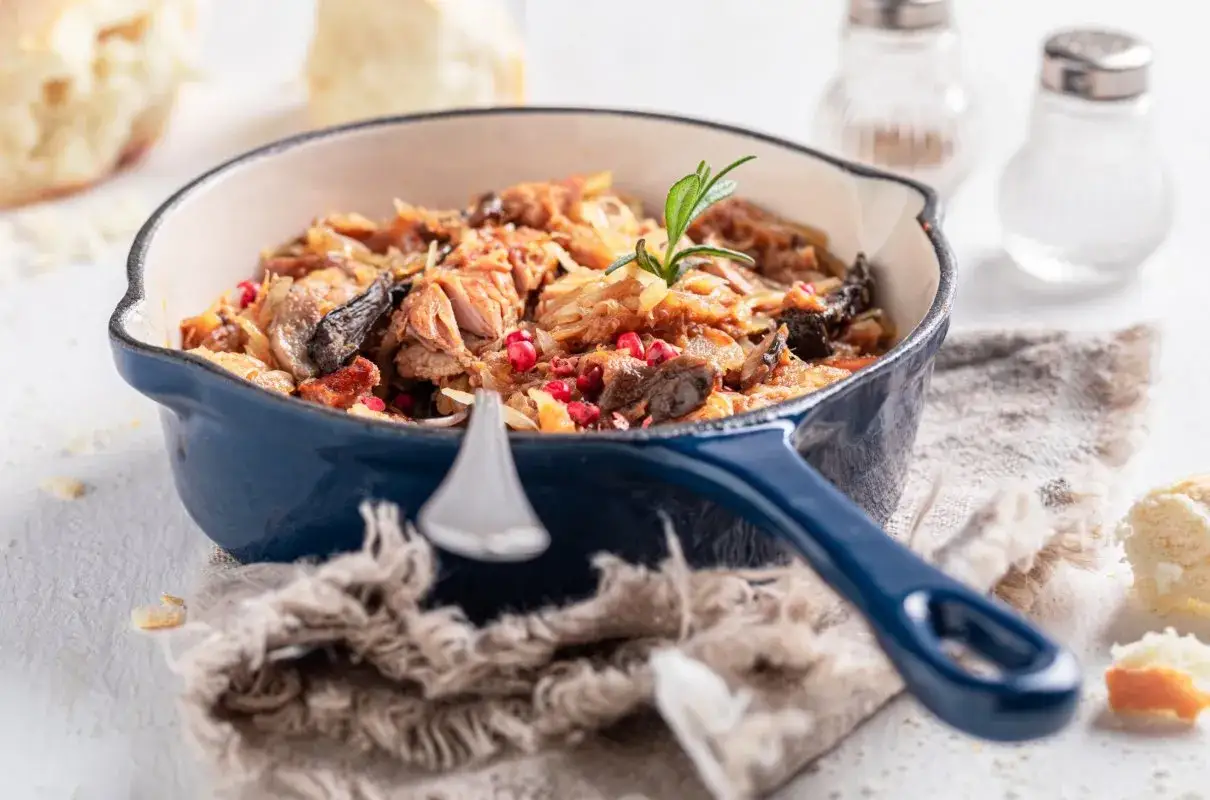 Ania gotuje pyszny bigos w niebieskim naczyniu, ozdobiony rozmarynem i żurawiną. Obok kromki chleba i solniczki.