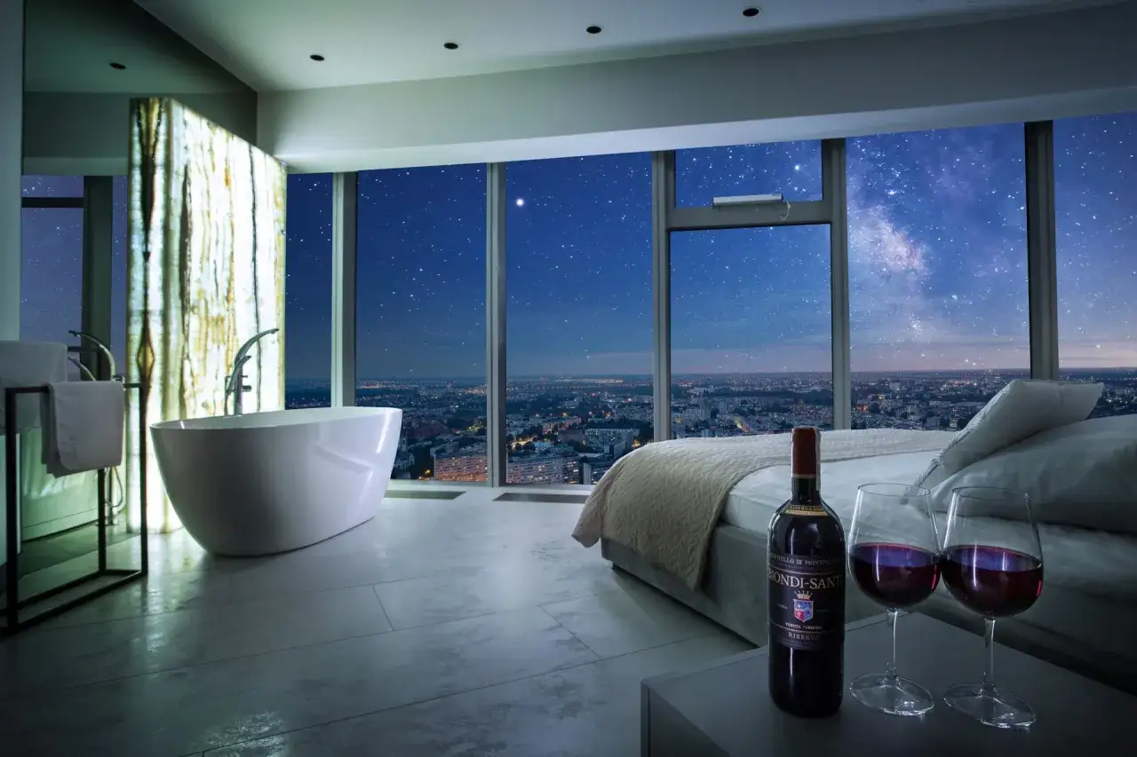 Luksusowy apartament suite z wanną i łóżkiem, z widokiem na nocne miasto i rozgwieżdżone niebo.