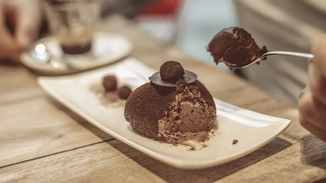Un delizioso tartufo alla nocciola, ricoperto di cacao, viene gustato con un cucchiaino. Altri tartufi e una tazzina di caff&egrave; completano la scena.