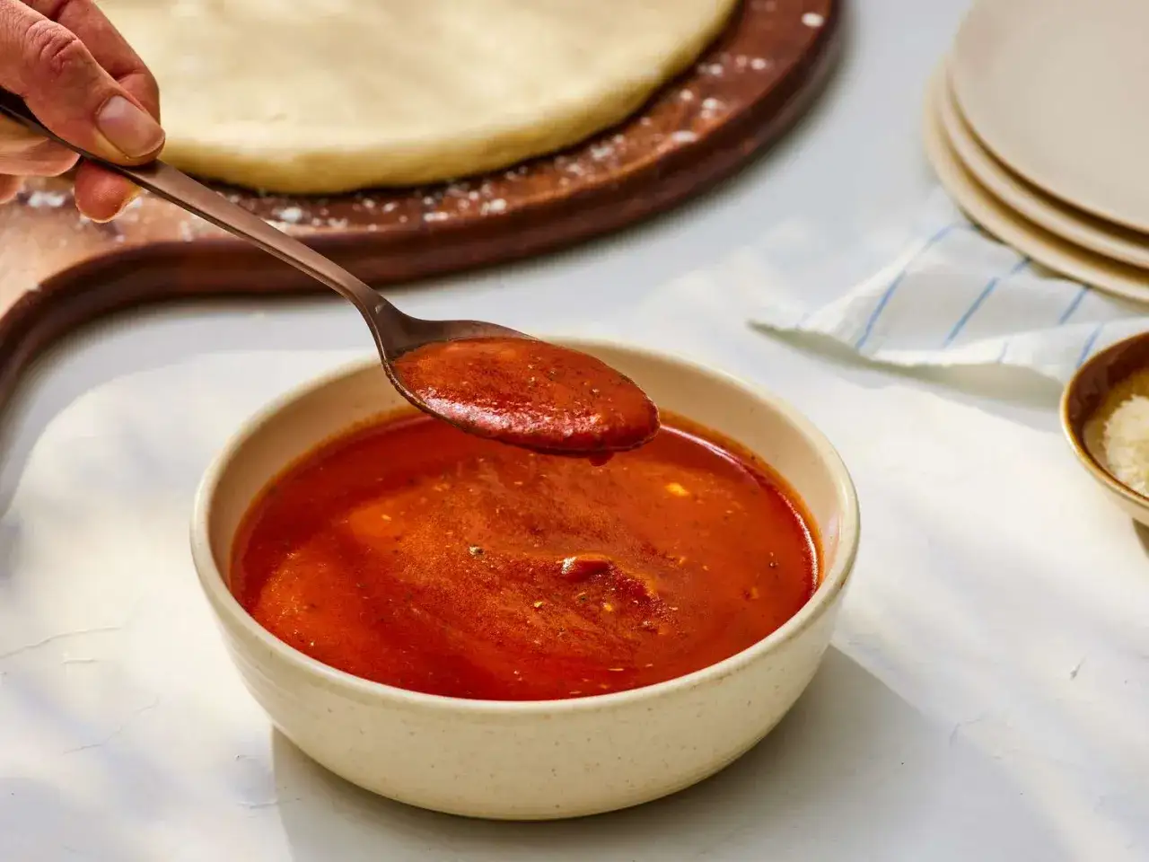 Gęsty, aromatyczny sos pomidorowy do pizzy, nabierany łyżką z miseczki. Obok ciasto na pizzę i starty ser.