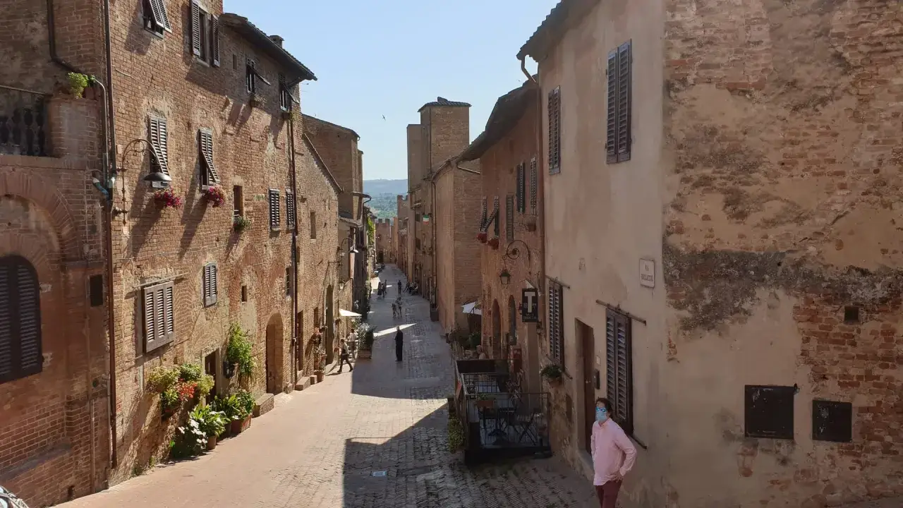 Un vicolo medievale a Certaldo, dove si trova il borgo antico con case in mattoni, finestre con persiane e fiori.