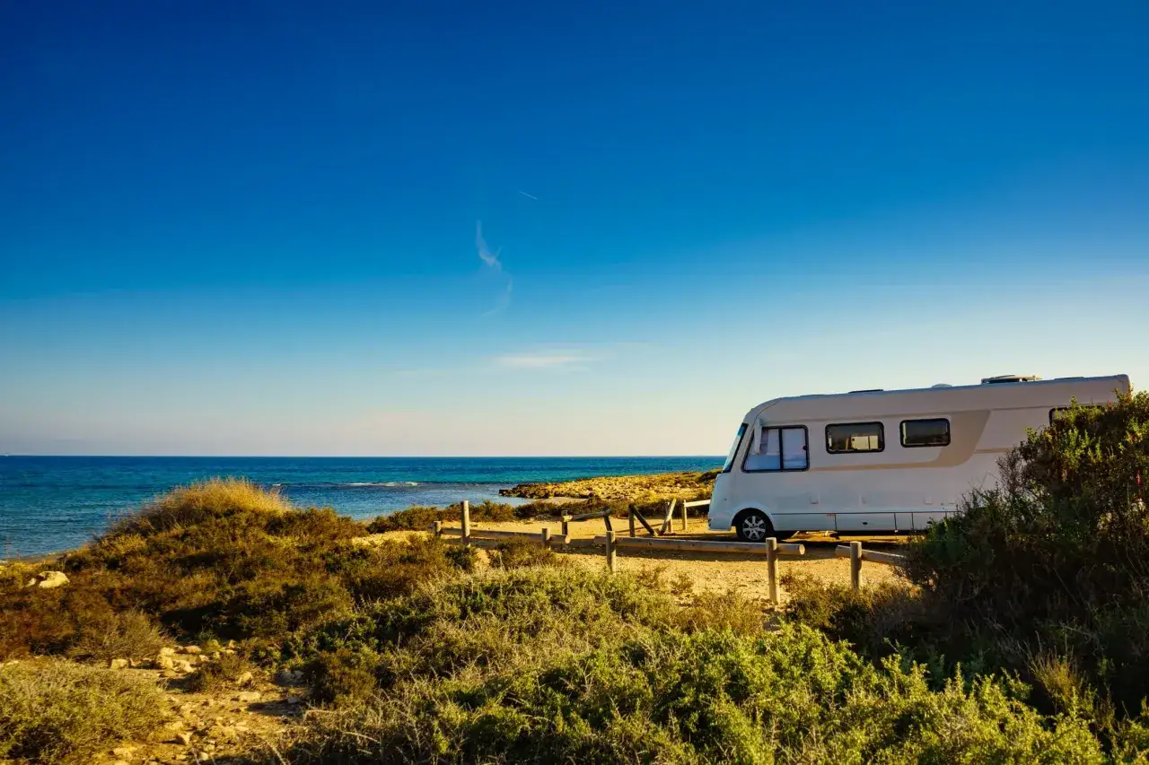 Un camper bianco sosta su un sentiero sterrato con vista sul mare blu intenso. Un'avventura indimenticabile in **Isola d'Elba in camper**.