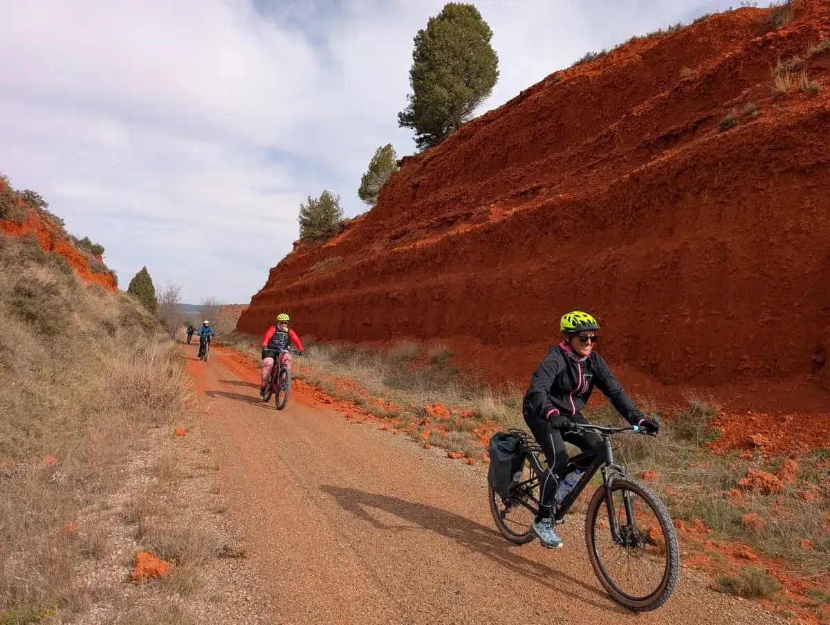 Ciclistas disfrutan de la vía verde en Valencia, rodeados de impresionantes formaciones rojas.
