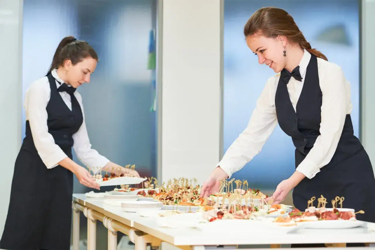 Dos camareras preparan canapés para un evento. Esto es food service: servicio de catering y atención al cliente.