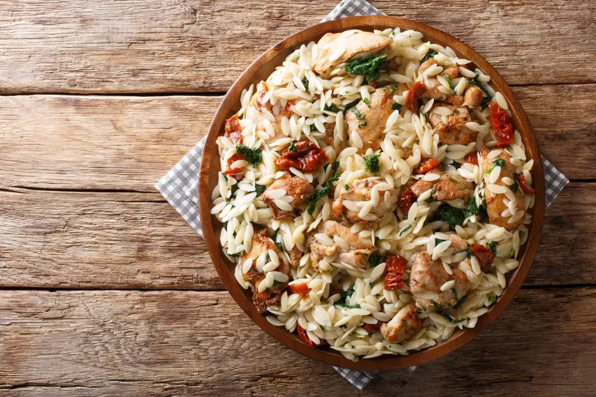 Pyszne danie z makaronem orzo, kurczakiem i suszonymi pomidorami na drewnianym stole.
