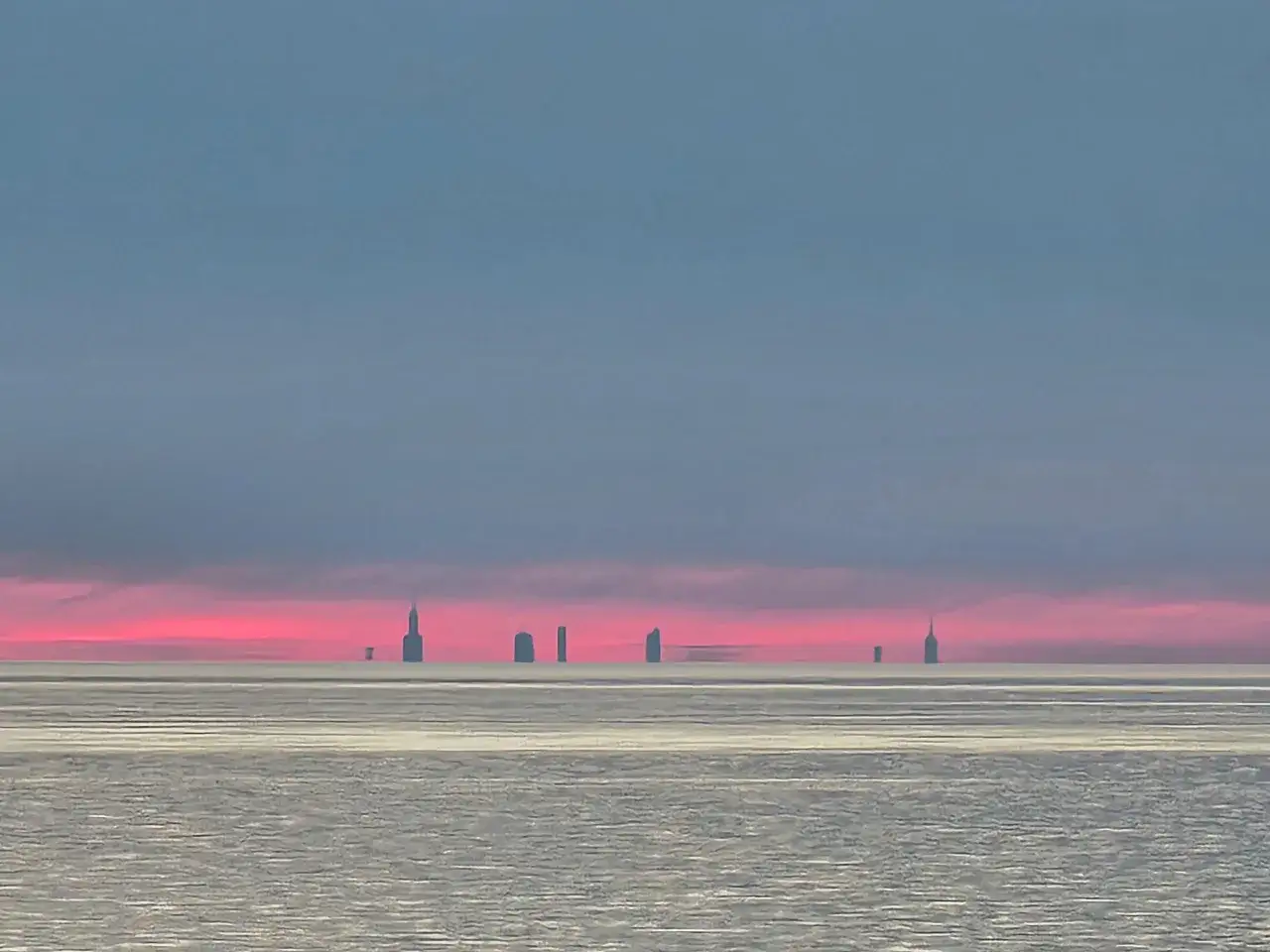 Silhouetted skyscrapers rise from the horizon over a vast, icy expanse under a vibrant pink and blue sky. This view makes you wonder, is Chicago worth visiting?