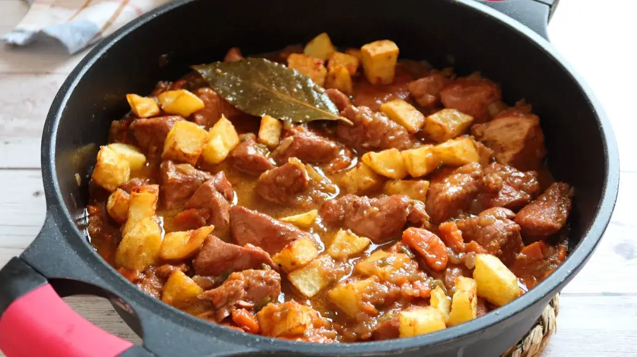 Guiso casero de osobuco de pavo con patatas y zanahorias, servido en una sartén negra.