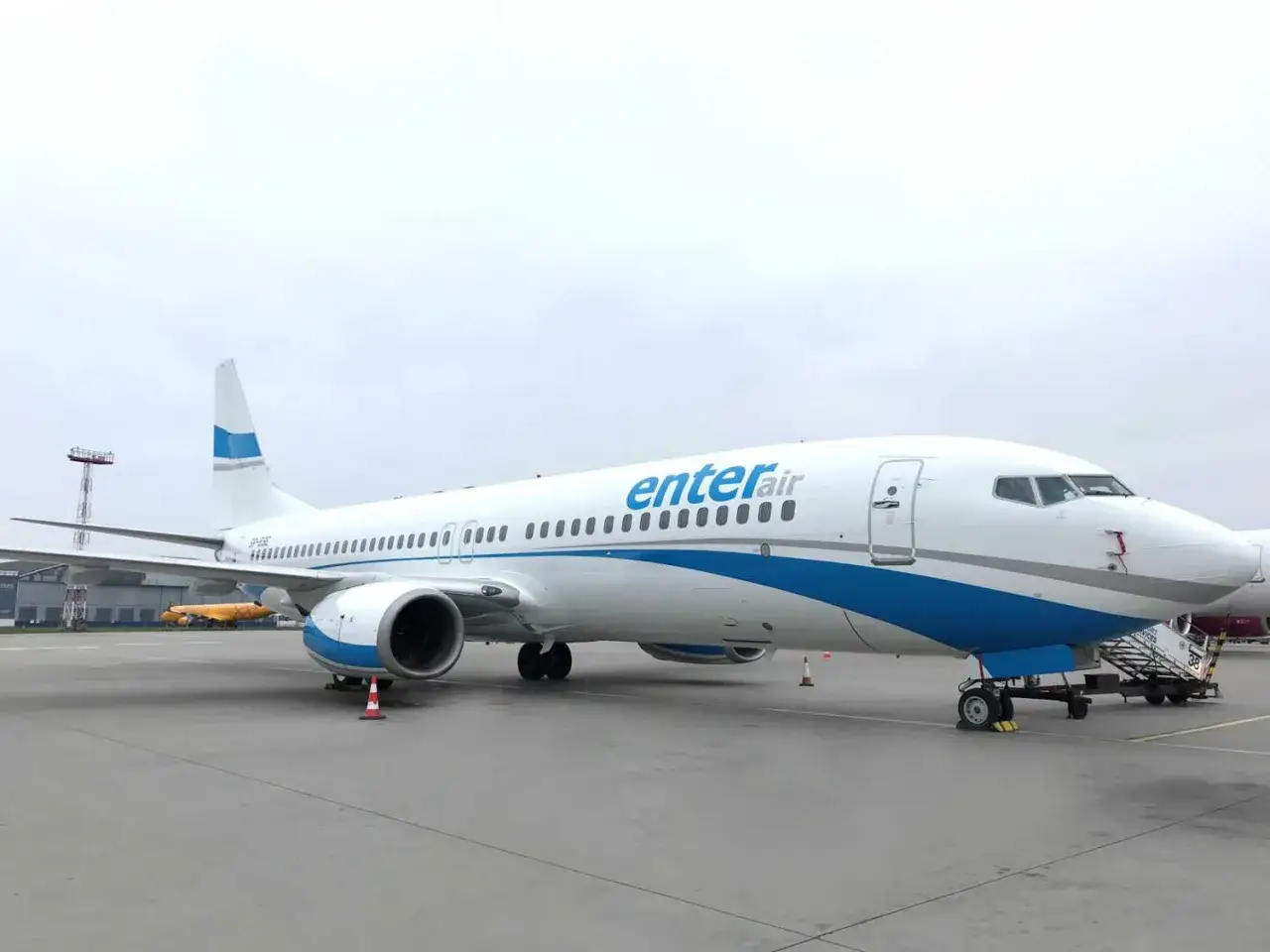 Biały samolot Enter Air z niebieskimi pasami na tle pochmurnego nieba. Gotowy do startu, by zabrać pasażerów w podróż.