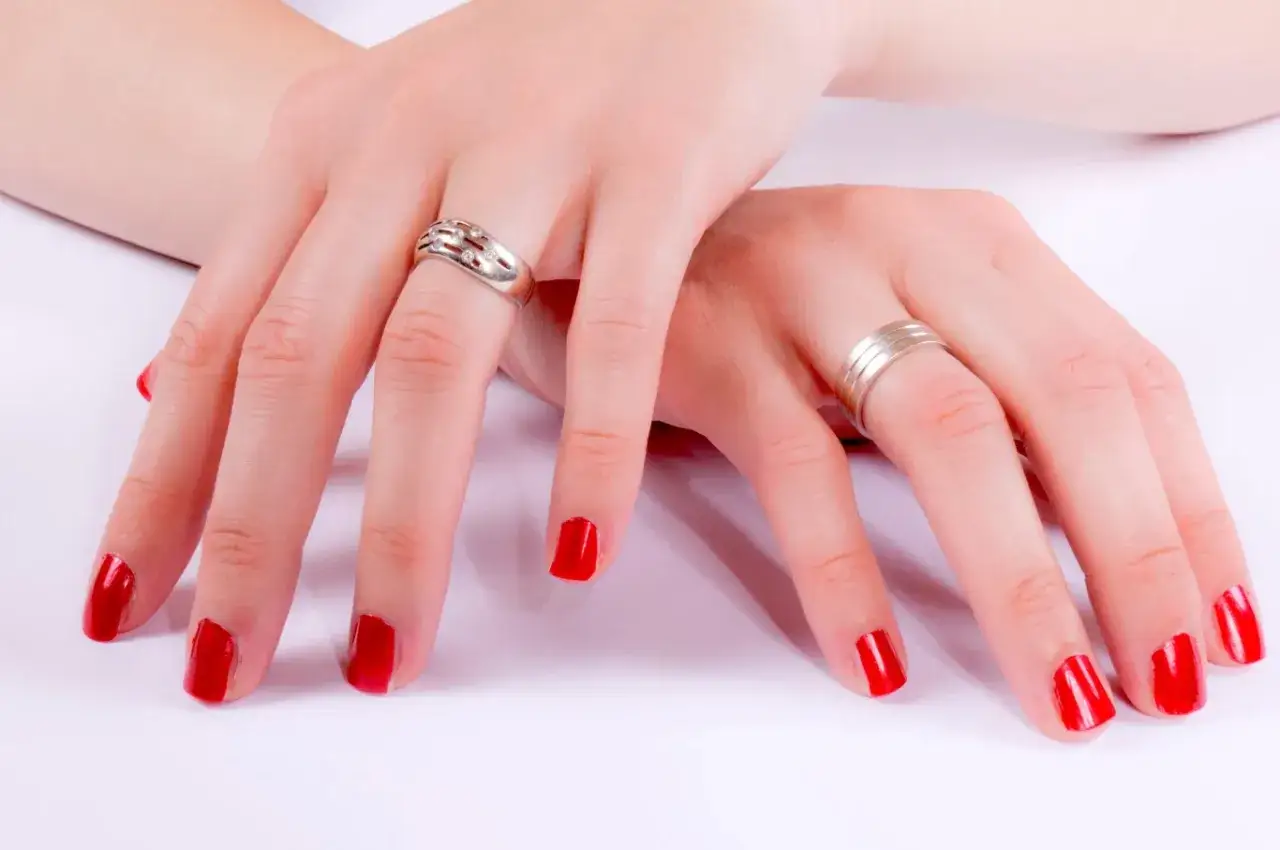 Dłonie z czerwonym lakierem do paznokci i pierścionkami. Czekam aż lakier do paznokci wyschnie, by móc cieszyć się idealnym manicure.