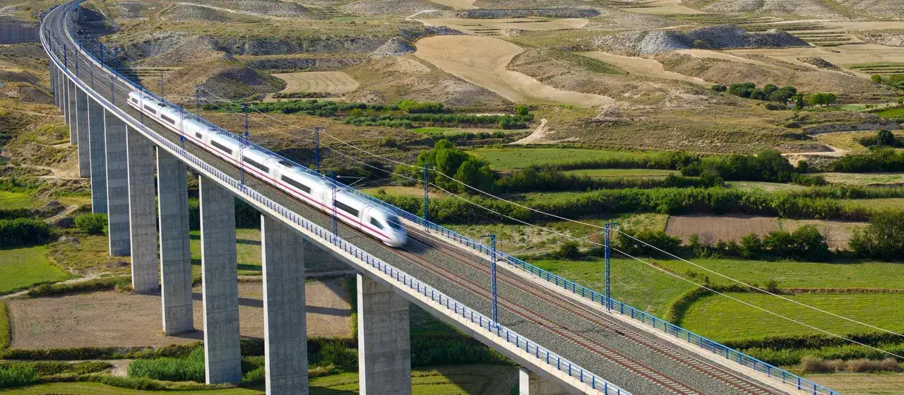 Un tren AVE cruza un viaducto sobre un paisaje rural, conectando la cuenca de Madrid con otros destinos.