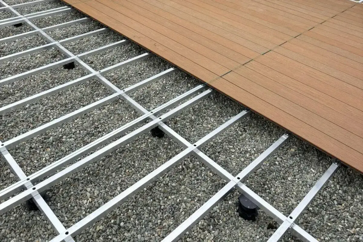 Montaż desek kompozytowych na aluminiowym ruszcie, pod kt&oacute;rym widać żwir. Trwa budowa tarasu.