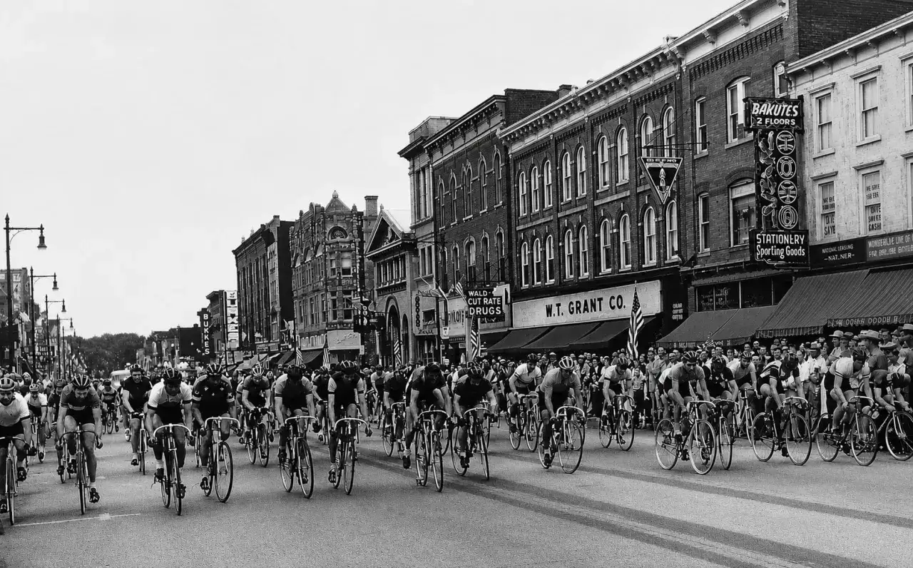 A lively bicycle race, part of a tour of Somerville, unfolds on a street lined with vintage shops and cheering crowds.