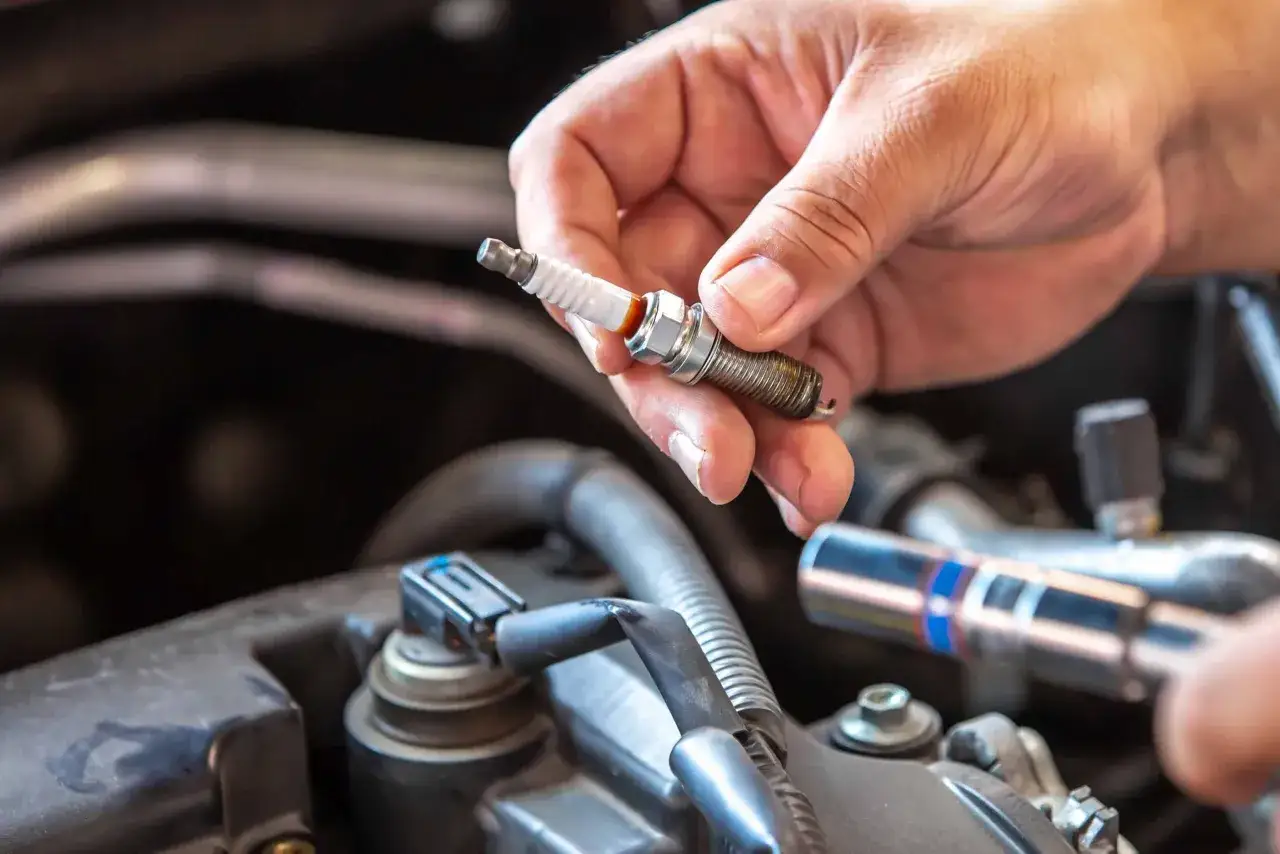 A hand holds a used spark plug, ready for replacement. This DIY task can significantly impact spark plug replacement cost.