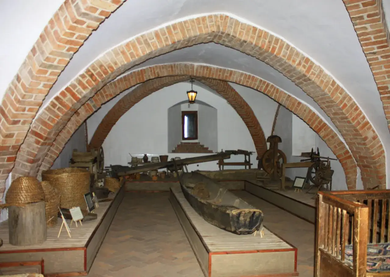 Wnętrze zamku Golub-Dobrzyń podczas zwiedzania. Widać tu łódź, kosze, narzędzia i ceramikę pod ceglanymi łukami.