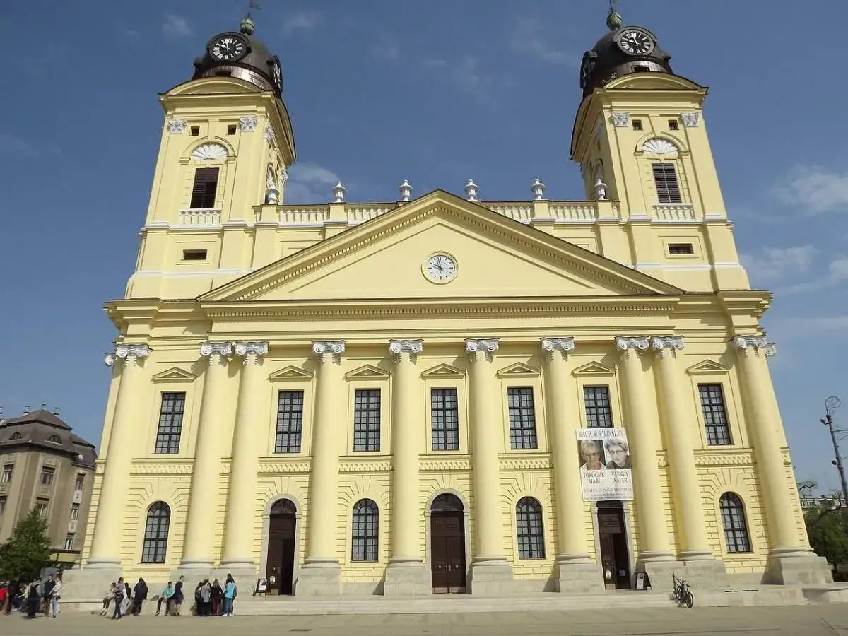 Debreczyn atrakcje: imponująca, żółta katedra z dwiema wieżami i zegarami. Na fasadzie wiszą plakaty zapraszające na wydarzenia kulturalne.