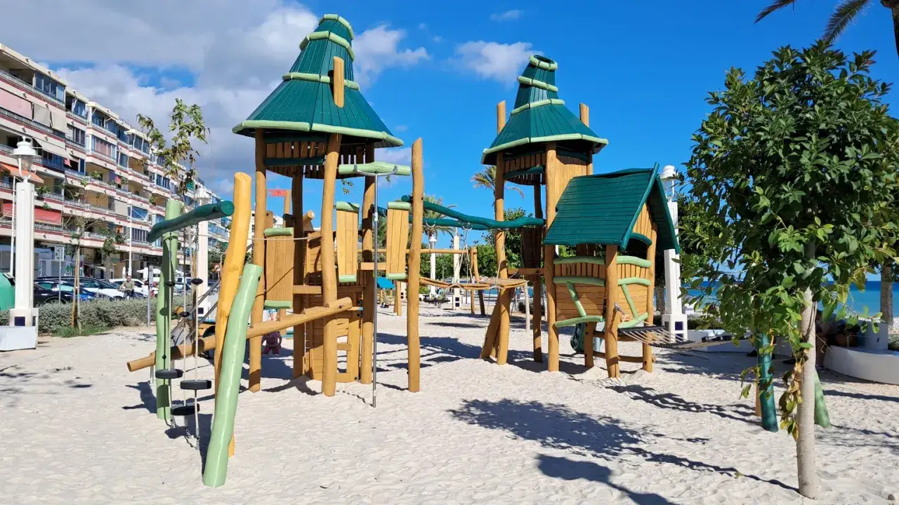 Parque infantil en Altea con estructuras de madera y tejados verdes, ideal para que los niños jueguen en la arena.
