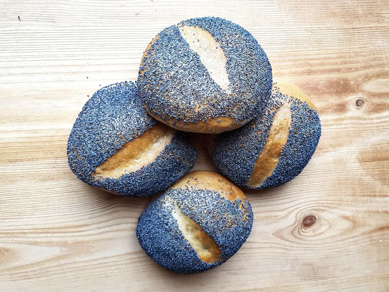 Vier Mohnbrötchen liegen auf einem Holztisch. Sind Mohnbrötchen gesund? Ja, Mohn ist reich an Nährstoffen.