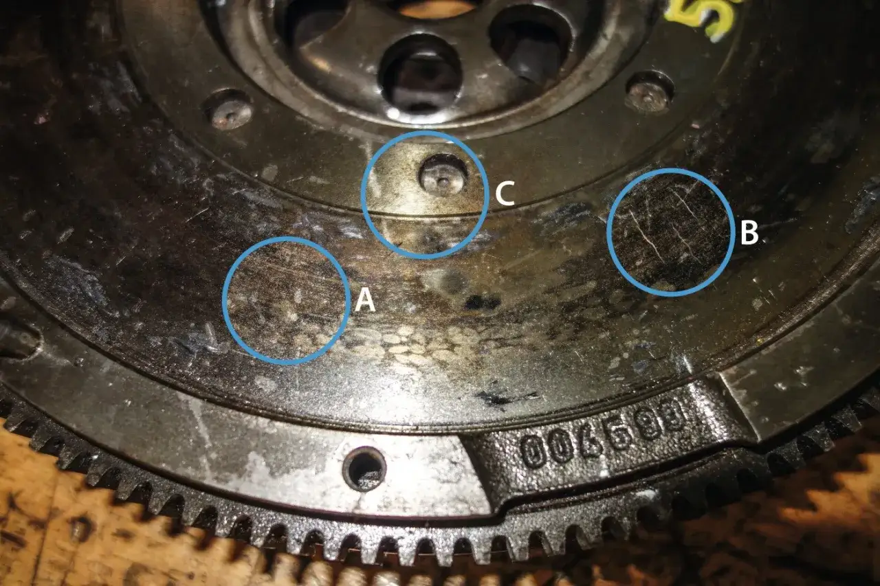 Nahaufnahme einer verschlissenen **Schwungscheibe Auto** mit markierten Bereichen (A, B, C), die Abnutzungsspuren und Kratzer zeigen.