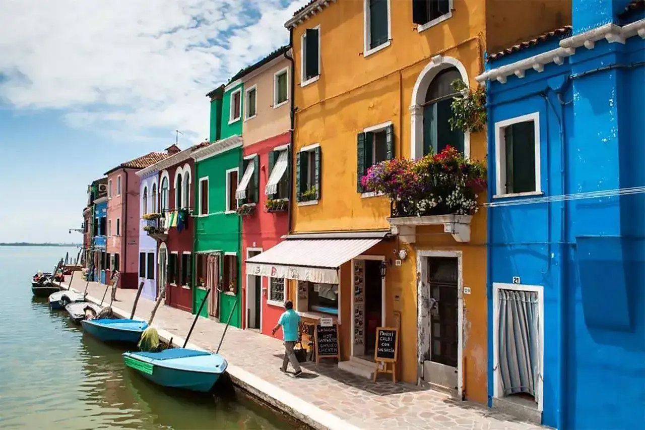 Case colorate a Burano, perfette per un free tour Venezia. Barche sull'acqua, fiori sui balconi, un'atmosfera da sogno.