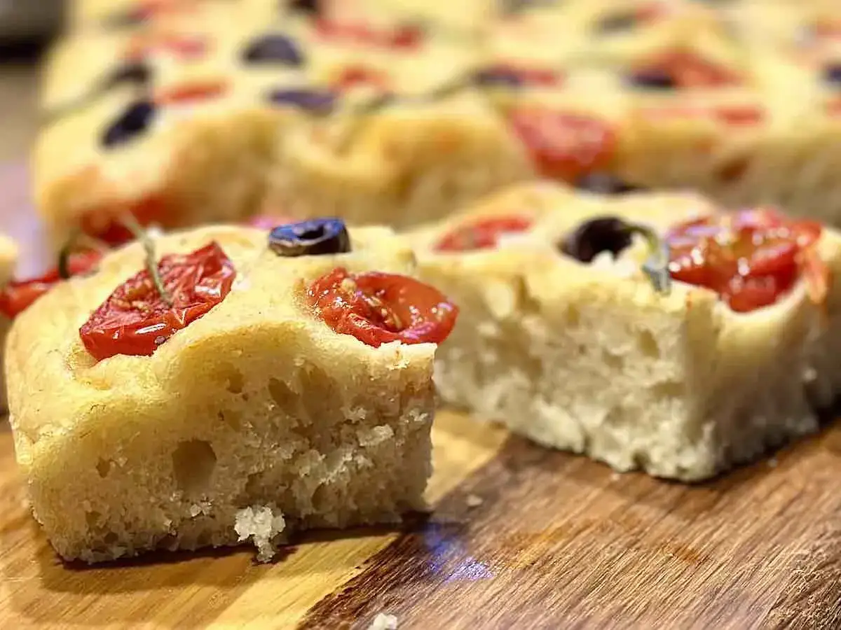 Pyszna włoska focaccia z pomidorkami i oliwkami, pachnąca ziołami. Idealna na przekąskę.