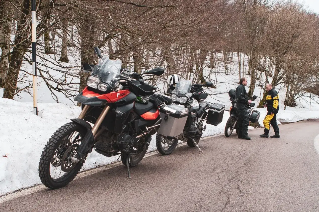 Sycylia pogoda wrzesień: motocykliści w górach, śnieg na poboczu, drzewa bez liści.