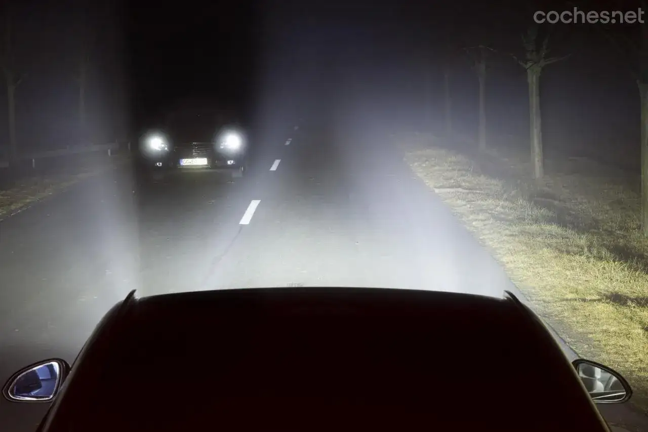 Conducir de noche en una carretera con niebla, con las luces de otro coche iluminando el camino.