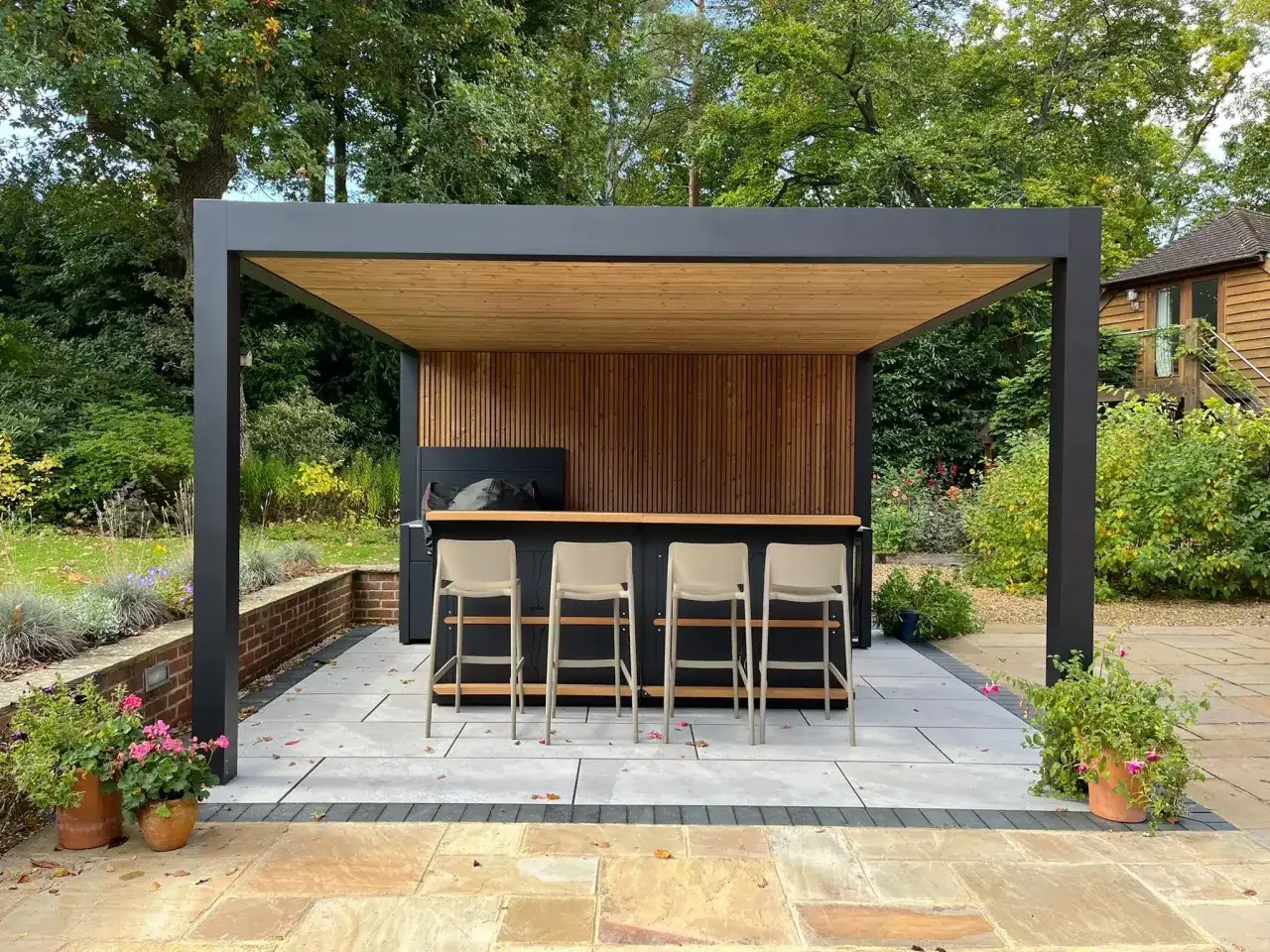 Une pergola moderne abrite un bar ext&eacute;rieur avec des tabourets. C'est un espace id&eacute;al pour se d&eacute;tendre et profiter du jardin.