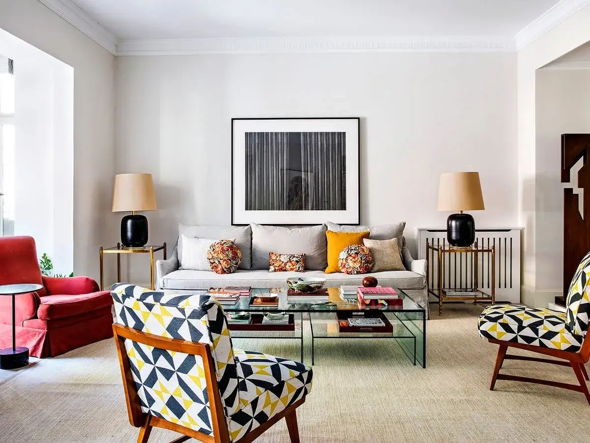 Sofá gris y butacas con estampado geométrico y floral, combinando estilos para un salón moderno.
