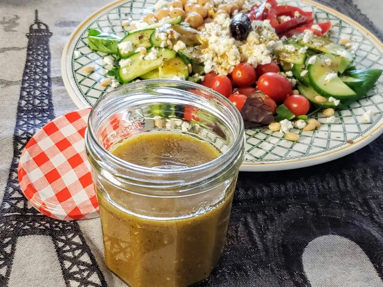 Ein Glas mit hausgemachtem French Dressing steht neben einem bunten Salat mit Feta, Tomaten und Gurken.